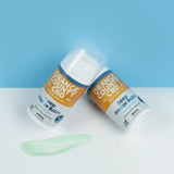Two tubes of Orange County CBD Deep Freeze Balm are shown on a white surface against a light blue background, with a pale green balm smear in front. The packaging features orange, white, and blue colors.