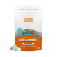 An orange and white stand-up pouch of Orange County CBD Gummies, shown on a clean white background with three loose gummies in front. The packaging features a clear window displaying multicolored gummies and includes text such as 'LAB TESTED | VEGAN | THC-FREE', '100 GUMMIES', and 'CBD GUMMIES'.