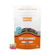 An orange and white stand-up pouch of Orange County CBD Gummies (Cherries) on a white background, with three cherry-shaped gummy candies displayed in the lower-left corner.