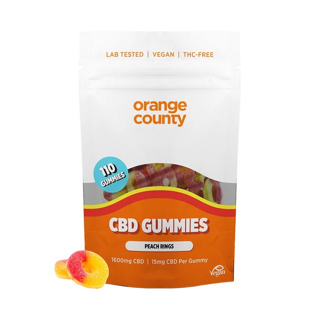 An orange and white stand-up pouch of Orange County CBD Gummies, labeled 'Peach Rings', with two gummy candies placed in front on a white background.