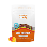 An orange and white stand-up pouch of Orange County CBD Gummies, labeled 'Peach Rings', with two gummy candies placed in front on a white background.
