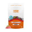 An orange and white stand-up pouch of Orange County CBD Gummies, Strawberry flavor, with three loose gummies displayed in front on a clean white background.