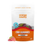 An orange and white stand-up pouch of Orange County CBD Gummies, Strawberry flavor, with three loose gummies displayed in front on a clean white background.