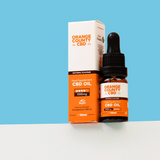 An amber glass dropper bottle of Orange County CBD Oil next to its white and orange cardboard packaging box, displayed on a white surface against a solid blue background.