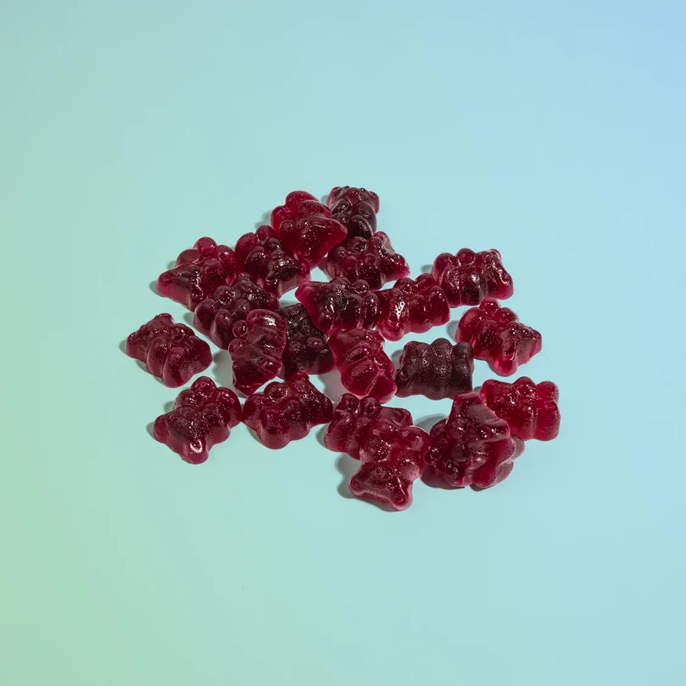 A pile of small translucent red gummy bear candies on a smooth light blue background.