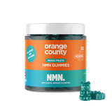 A jar of Orange County NMN Gummies for mixed fruits, featuring a bright orange and teal label with a white lid, shown alongside three green gummy bear candies on a white background.