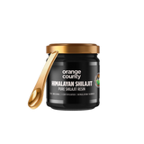 A jar of Orange County Himalayan Shilajit resin with a black body, gold lid, and a gold spoon resting against the jar, shown on a plain white background.